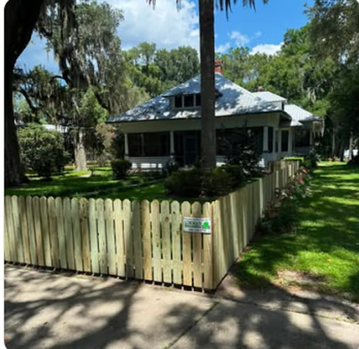 Wood picket fence running along the frontage of an older Florida home under live oaks