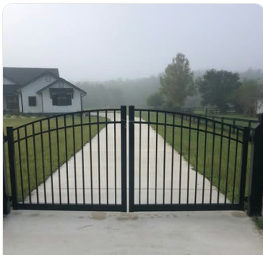 Black aluminum arched double drive gate closed across a residential driveway in morning fog